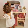 A young child is playing with a large wooden dollhouse. Voir les images du produit