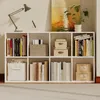 A white modular bookshelf filled with books and decorative boxes, with a desk lamp and a painting on top. Podgląd zdjęcia produktu