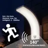 A dark outdoor scene at dusk or night, with a modern white LED wall light mounted on a brick wall. The light is illuminated, casting a bright glow. A silhouette of a running person and motion sensor waves are depicted, along with text detailing the light's Produktbild-Vorschau