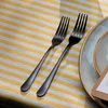 Two black forks are placed on a yellow and white striped tablecloth next to a plate. Podgląd zdjęcia produktu