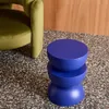 A blue stool is placed on a speckled floor next to a green armchair. The background is a wooden wall. Anteprima dell’immagine prodotto