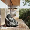 A bean bag chair and a small round table are placed on a wooden deck next to a house with large windows and a stone wall covered in ivy. Podgląd zdjęcia produktu