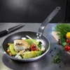A de BUYER CHOC RESTO pan filled with cooked fish and vegetables, placed on a stainless steel countertop next to a knife and fresh produce. Podgląd zdjęcia produktu