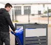 A man is putting a blue trash bin into a gray metal trash bin enclosure. Náhled obrázku produktu