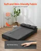A gray convertible sofa bed is laid out flat on a wooden floor, with three pillows at the head. The background is a plain white wall with a potted plant and curtains. Voir les images du produit