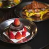 A close-up of a dessert with strawberries and a croissant in the background. Náhled obrázku produktu