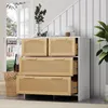 A chest of drawers with rattan fronts is placed next to a staircase, with a doorway and plants visible.