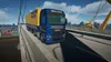 A blue and yellow truck is driving on a bridge over a body of water with ships and a city skyline in the background. Anteprima dell’immagine prodotto