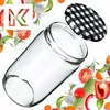 A clear glass jar with a black and white checkered lid, surrounded by various fresh vegetables and herbs. Podgląd zdjęcia produktu