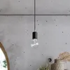 A close-up shot of a black pendant light with a clear Edison bulb hanging against a textured concrete wall. Anteprima dell’immagine prodotto