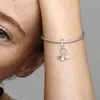 A close-up of a person's arm wearing a silver Pandora charm bracelet with three charms. Anteprima dell’immagine prodotto