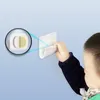 A child's hand is reaching for a white smartphone wall mount. A magnified view shows the adhesive backing. Produktbild-Vorschau