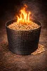 A black basket filled with wood pellets, with flames burning on top, placed on a textured brown surface. Produktbild-Vorschau