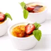 Three ceramic ramekins filled with crème brûlée, each garnished with a strawberry slice and a mint leaf, are arranged on a white surface. Anteprima dell’immagine prodotto