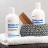 Two bottles of Healpsorin shampoo and conditioner are displayed on towels, with a wooden comb in a knitted basket. Podgląd zdjęcia produktu