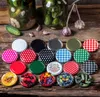 A collection of jar lids and some jars with pickles and garlic on a wooden surface. Anteprima dell’immagine prodotto