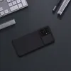 A black phone case with a camera cover is placed on a dark surface, next to a keyboard and a USB drive. Náhled obrázku produktu