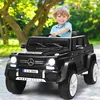 A young boy is sitting in a black toy Mercedes-Benz G-Wagon in an outdoor setting with trees and foliage in the background. Produktbild-Vorschau