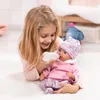 A young girl is feeding a baby doll with a bottle while lying on a white rug. Produktbild-Vorschau