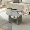 A round, light gray coffee table is placed on a patterned rug in front of a sofa. A vase with pink flowers and a cup of coffee on a magazine are on the table. Produktbild-Vorschau