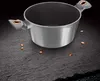 A silver pot with gray and copper handles sits on a dark, textured surface, with small copper-colored pieces scattered around it. Náhled obrázku produktu
