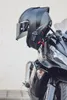A black motorcycle helmet with a communication system attached is mounted on a motorcycle. Produktbild-Vorschau