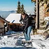 A man is shoveling snow in a snowy environment with wooden houses in the background. Produktbild-Vorschau