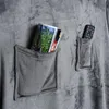 Close-up of a gray blanket with two pockets. One pocket contains magazines, and the other contains a remote control. Produktbild-Vorschau