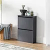 A gray shoe cabinet with two flip-down doors, decorated with small potted plants on top, stands next to a woven basket filled with blankets and pillows. Produktbild-Vorschau