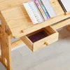 A close-up view of a wooden desk with an open drawer containing a book and a watercolor paint set on the surface. Produktbild-Vorschau