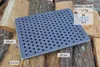 A cast iron grate with holes is placed on a pile of firewood. Produktbild-Vorschau