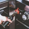 A hand is opening a bottle of beer with a bottle opener attached to a grill. Anteprima dell’immagine prodotto