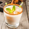 A close-up of a creamy drink with a cinnamon rim and mint garnish, served in a glass with a striped straw. Produktbild-Vorschau