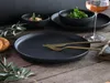A table setting with dark plates, cutlery, and a glass of wine. Podgląd zdjęcia produktu