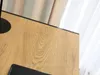 A close-up view of a wooden desk surface with a black edge, with curtains in the background. Náhled obrázku produktu