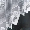 A close-up view of a white lace curtain with floral and scroll patterns. Produktbild-Vorschau
