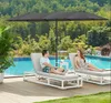 A couple relaxing on lounge chairs under a large umbrella next to a swimming pool. Produktbild-Vorschau