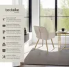 A beige upholstered chair with gold legs is placed next to a small round table in a well-lit room with a large window overlooking a forest. Produktbild-Vorschau