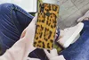 A person holding a phone with a leopard print case while sitting down. Produktbild-Vorschau