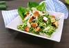 A close-up of a Caesar salad with chicken and croutons served in a white square bowl, with a blue and white striped napkin in the background. Produktbild-Vorschau