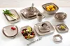 A collection of ceramic tableware, including plates, bowls, and a mug, arranged on a white surface. Produktbild-Vorschau
