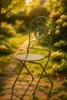 A vintage-style metal chair sits on a brick path in a garden setting. Produktbild-Vorschau