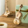 A wooden model of a cello and a model of the Eiffel Tower are displayed on a wooden table next to a gift-wrapped box. Anteprima dell’immagine prodotto