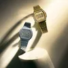 Two digital watches, one gold and one silver, are displayed on a light-colored surface with dramatic shadows. Produktbild-Vorschau