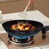 A hand is using a spatula to stir food in a black wok on a gas stove. Podgląd zdjęcia produktu