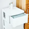 A white plastic drawer cabinet with a blue towel in one of the drawers, placed next to a wooden cabinet. Produktbild-Vorschau