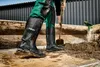 A person wearing black work boots and green overalls is digging in dirt with a shovel. Produktbild-Vorschau