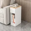 A narrow white side table with a wood-effect top is placed next to a sofa, with books on the lower shelf and a magazine and cup on the top. The floor is tiled. Produktbild-Vorschau