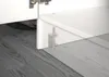A close-up view of a white cabinet or furniture piece with a metal bracket and pin attached to the floor. Produktbild-Vorschau