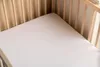 A close-up view of a white crib sheet inside a wooden crib. Produktbild-Vorschau